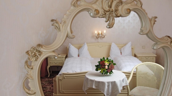 Відображення ліжка у великому декоративному дзеркалі, приклад розташування дзеркала навпроти спального місця в класичному інтер'єрі спальні.